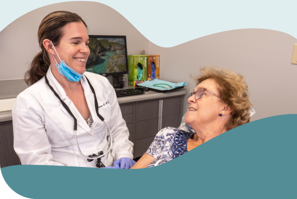 A smiling dentist speaks warmly with an older patient in a dental office, representing compassionate general and family dentistry with expertise in periodontal dentistry.
